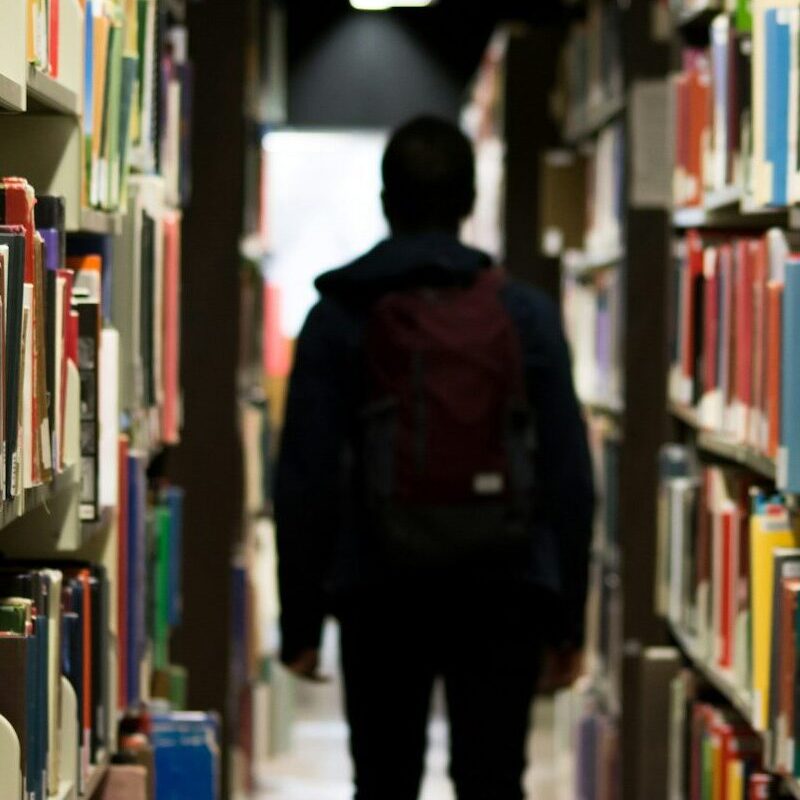 man with backpack beside a books